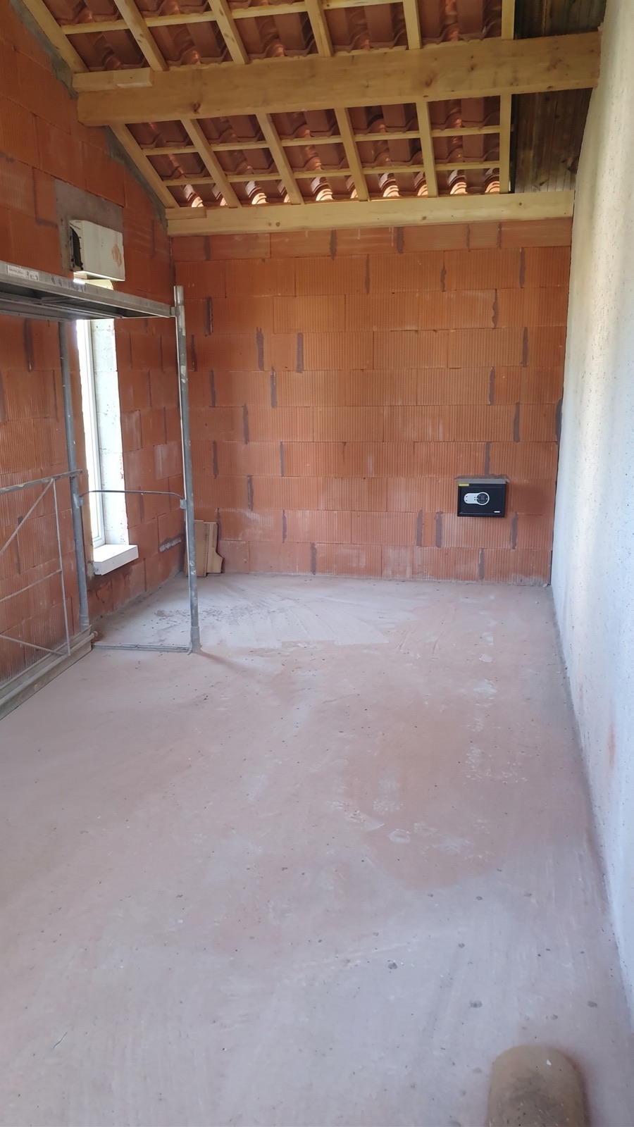 Pièce en cours de maçonnerie : murs en brique, charpente apparente et coffre-fort encastré dans le mur